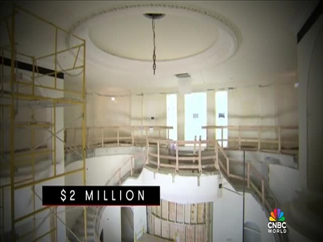 A partially constructed interior, possibly a theater, is visible with scaffolding and wooden railings. The CNBC World logo appears in the corner, and a graphic states "$2 MILLION."
