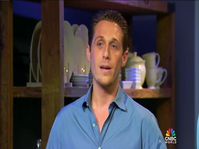 A man in a blue shirt is speaking, framed against a backdrop of shelves and dishes on CNBC World. The logo is visible in the bottom right corner.

