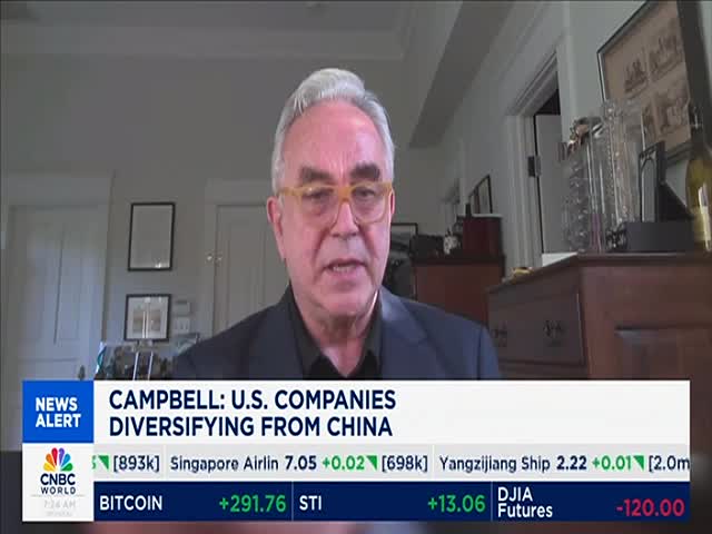 A man with glasses speaks directly into the camera, his words likely about U.S. companies. CNBC World's ticker tape scrolls beneath him, displaying financial data.
