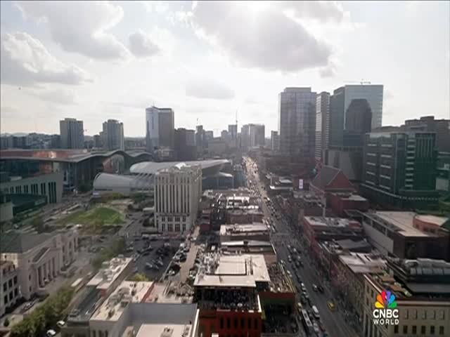 Traffic crawls along a long city street, flanked by tall buildings and the occasional park. The CNBC World logo is visible in the bottom right corner, framing the urban landscape.
