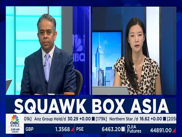 Two anchors sit at their desks, each looking directly at the camera. A lower third graphic displays the CNBC World logo and stock market data.
