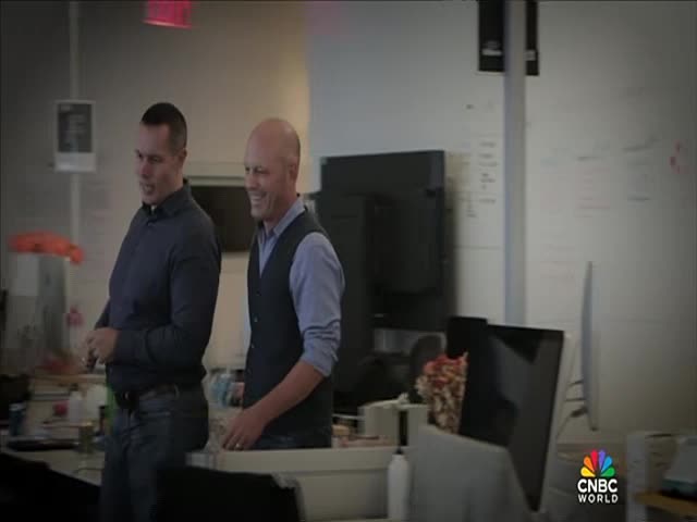 Two men, dressed in business casual, walk through an office, smiling. The CNBC World logo is visible in the corner.
