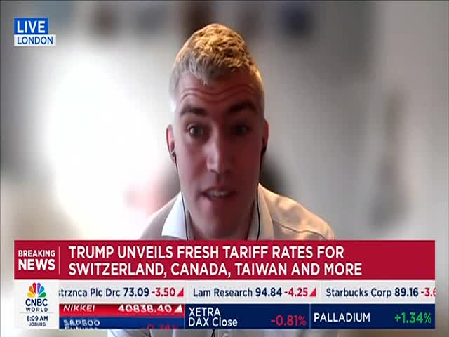 A man with short, light-colored hair is speaking on CNBC World, the "Breaking News" banner flashing below him. Headlines announce fresh tariff rates from Trump, with stock market data scrolling at the bottom of the screen.
