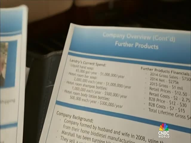 A printed page with financial data, including "Landry's Current Spend," is displayed on CNBC World. The document lists expenses for products like liquid hand soap and shampoo bottles.
