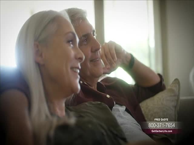 A smiling older couple sits close together, looking off to the right. The man has an arm resting on a pillow, and a phone number flashes at the bottom of the screen.
