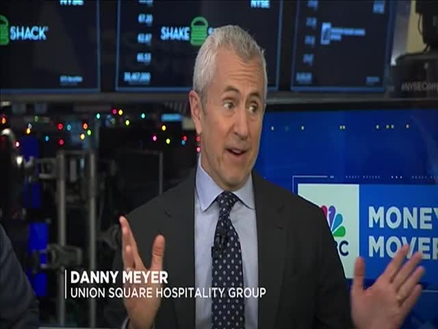 A man in a suit, identified as Danny Meyer, gestures animatedly on a CNBC set. Behind him, screens display stock information and the CNBC logo.

