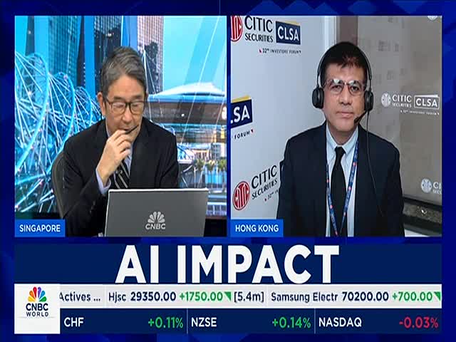 Two men in suits are on CNBC World, one in Singapore and the other in Hong Kong. The screen displays stock market updates below the "AI IMPACT" headline.

