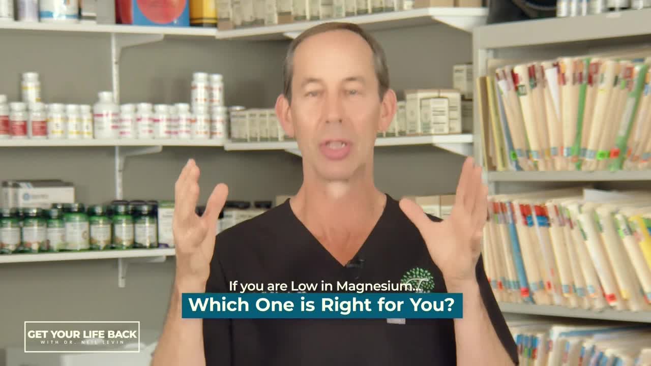 A man in a black scrub top gestures with both hands, speaking directly to the camera. Behind him, shelves are stocked with pill bottles and files.
