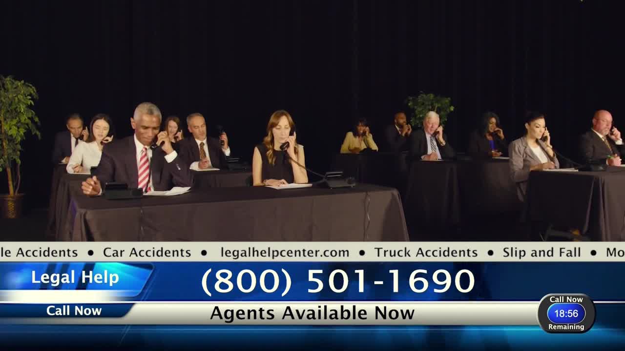 A dozen people sit at desks, holding phones to their ears. A graphic at the bottom of the screen advertises legal help, with a phone number and a timer counting down.
