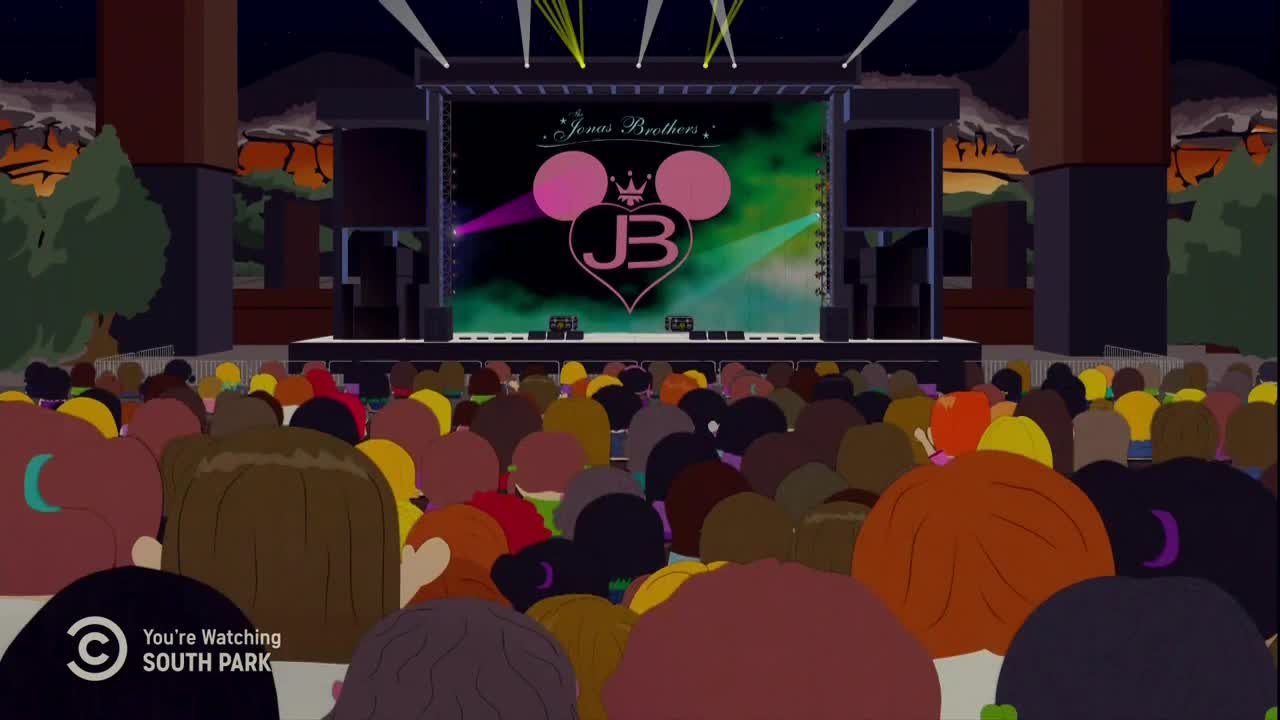 The crowd is packed, facing a stage lit with the Jonas Brothers' logo. Light beams sweep across the screen, and the audience is a sea of heads.
