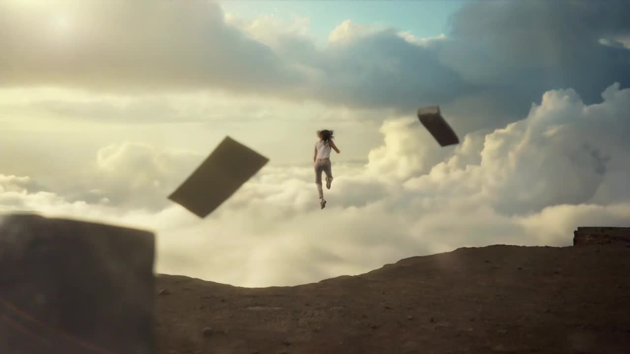 A person is running in mid-air, legs pumping, with a few rectangular objects floating nearby. The scene takes place above the clouds, with the ground visible below.
