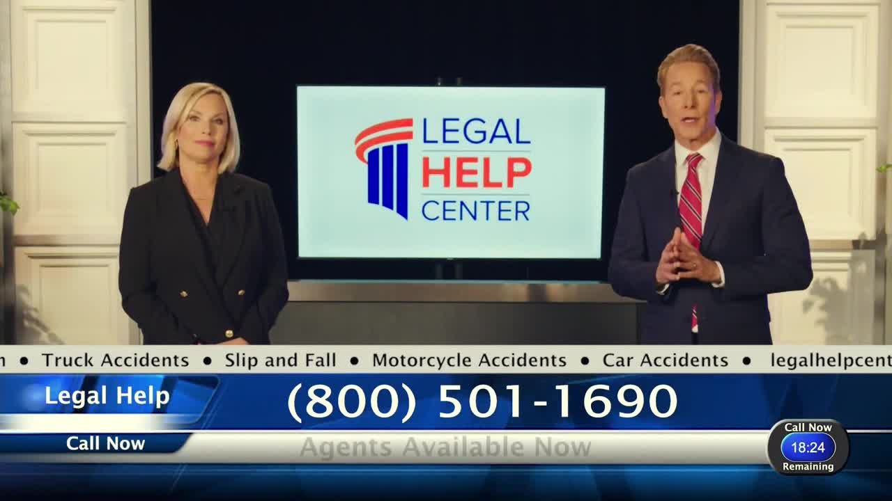 Two people in suits stand in front of a screen with a "Legal Help Center" logo. A phone number and the words "Agents Available Now" are displayed at the bottom of the screen.
