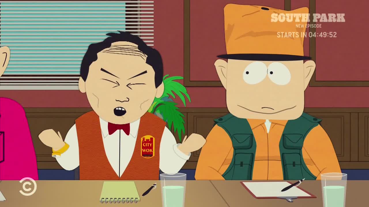 The man in the City Wok uniform is gesturing wildly, his eyes squeezed shut as he speaks. Beside him, a man in an orange outfit and hat stares blankly.
