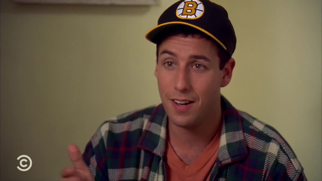 The man in the Bruins cap is mid-sentence, gesturing with his right hand. A Comedy Central logo is visible in the corner, likely from a show in the United States.
