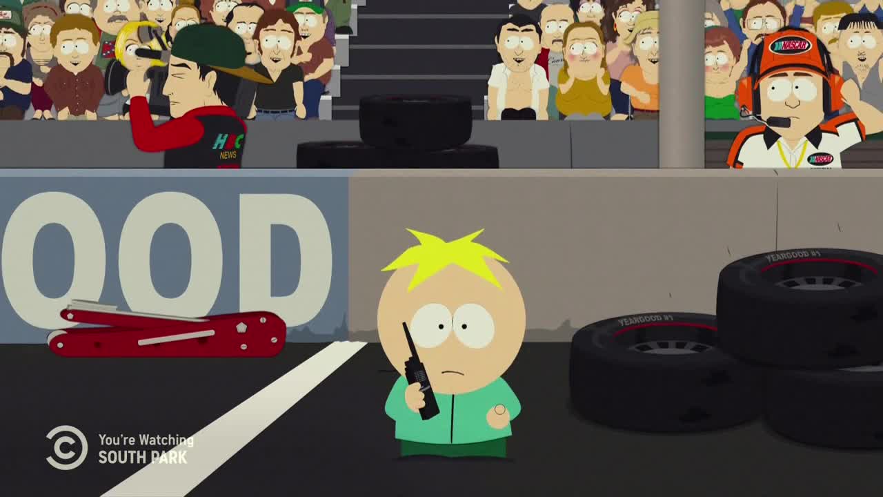 Butters stands with a walkie-talkie, looking concerned as he watches the race. A NASCAR official in a headset gestures from the pit crew, and a news reporter holds a camera.
