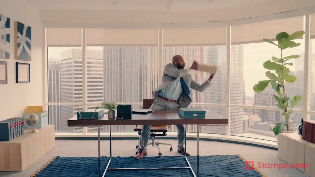 A man in a suit is flailing, mid-air, a file folder in his hand. He's in an office with a city skyline visible through the windows.
