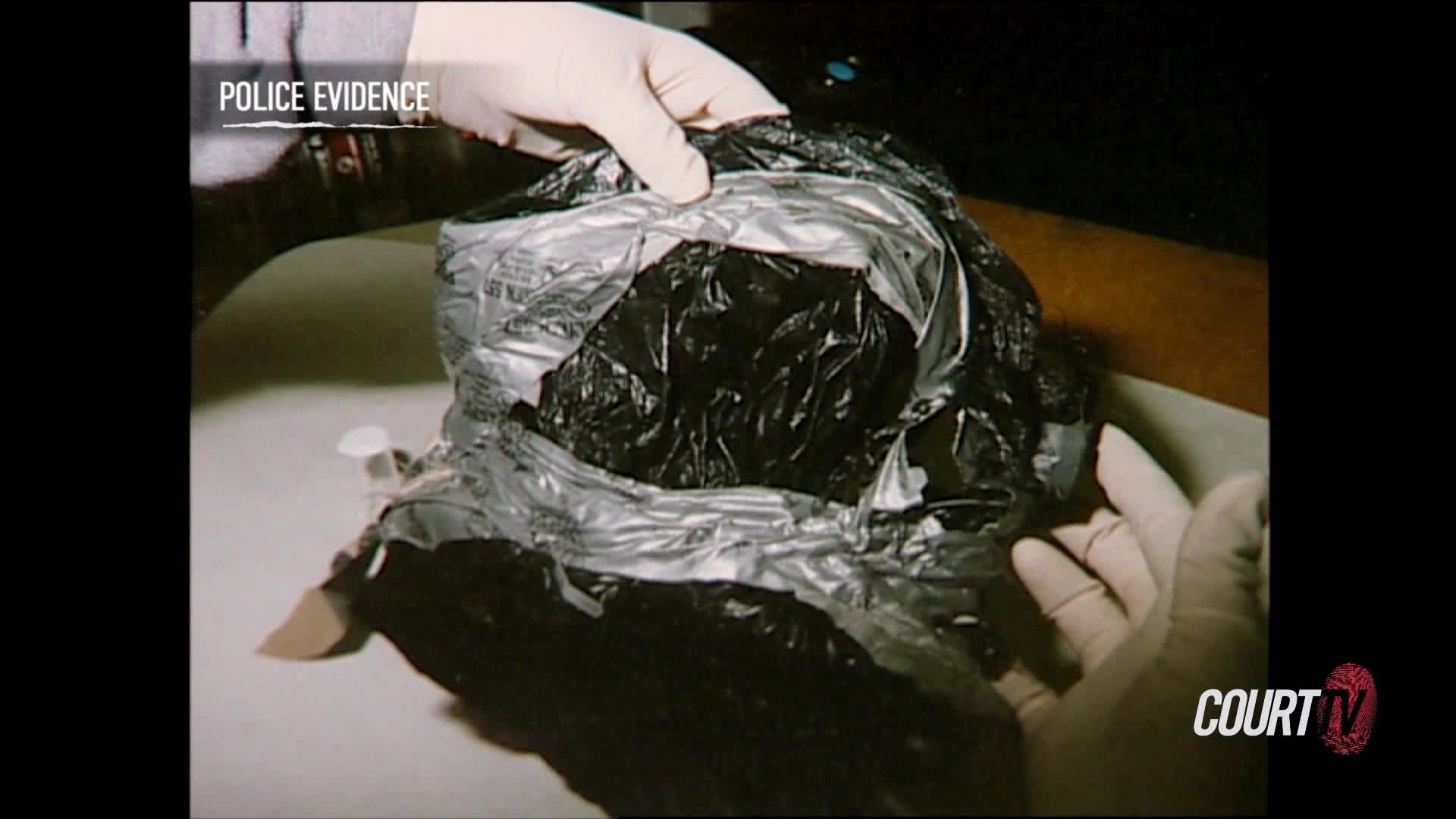 Gloved hands are carefully pulling open a black plastic bag, revealing a dark, crumpled interior. The scene is labeled "Police Evidence" on the Court TV broadcast.
