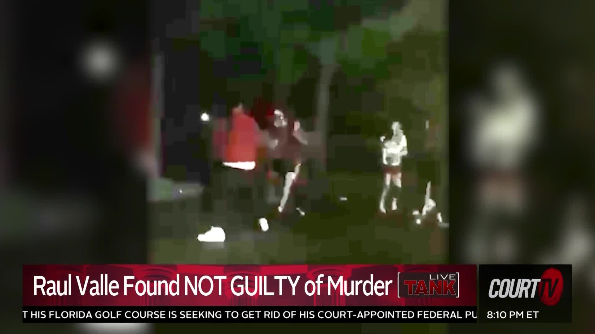 A group of people are tussling on the grass, illuminated by a dim light source. Someone in a red jacket is in the thick of it, while another person stands to the side, watching.
