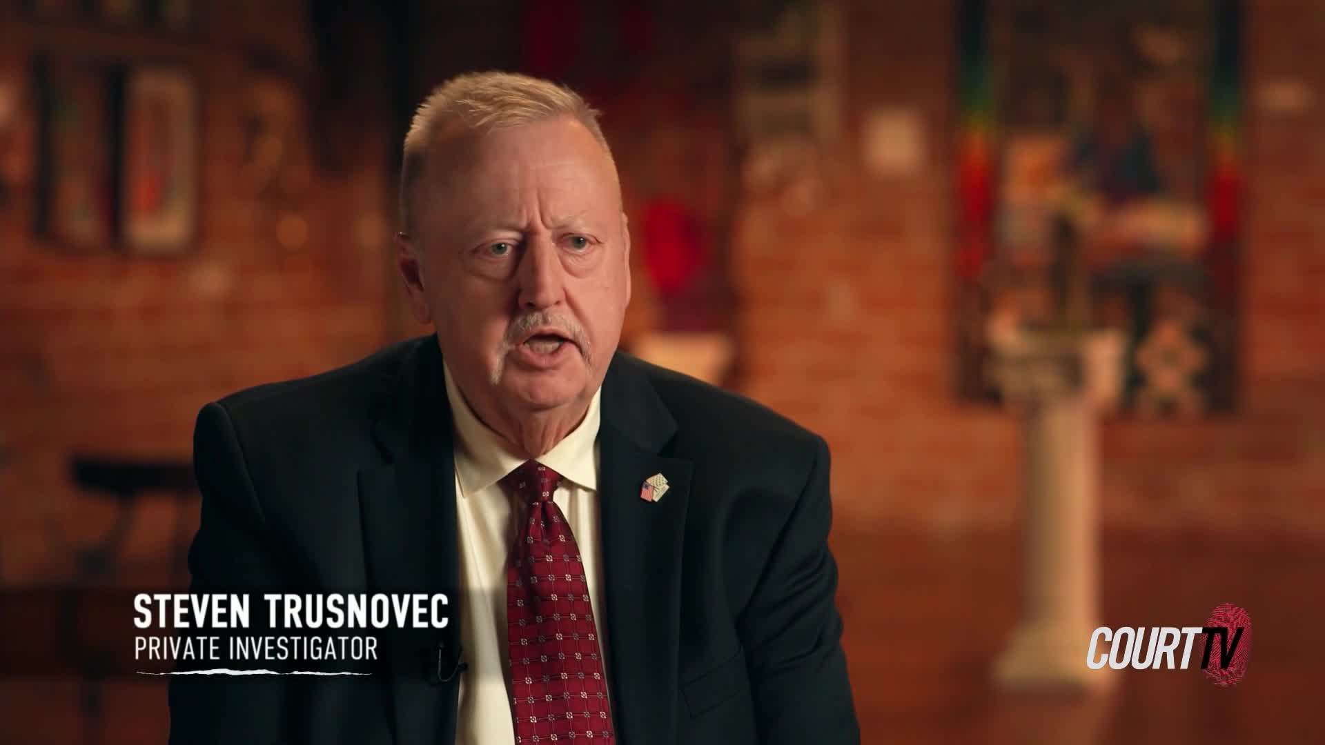 Steven Trusnovec, a private investigator, is speaking directly to the camera. His mouth is open, and he's wearing a dark suit and a patterned red tie.

