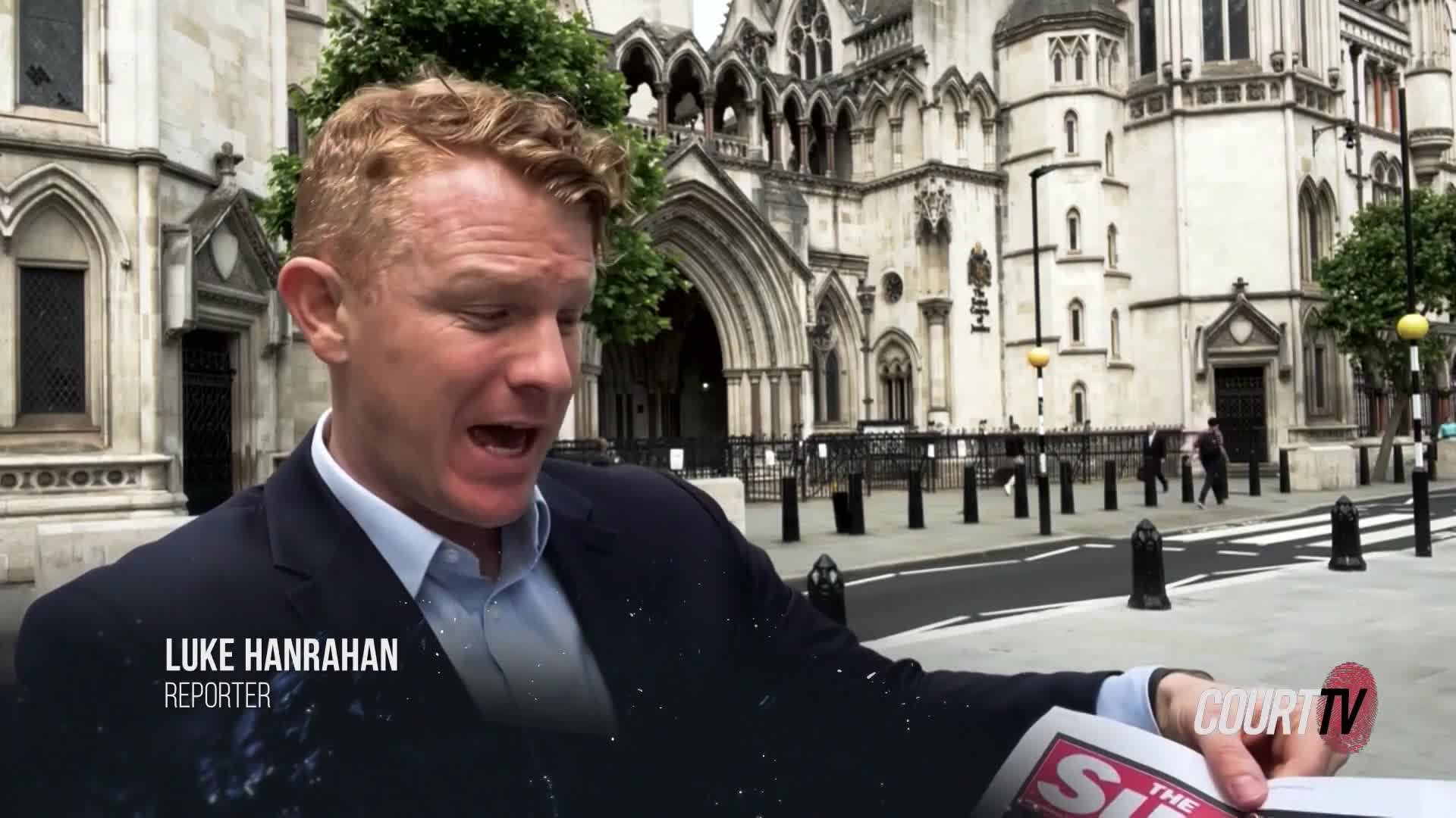 Luke Hanrahan, a Court TV reporter, is speaking animatedly in front of a grand building. He's holding a newspaper, gesturing with it as he reports.
