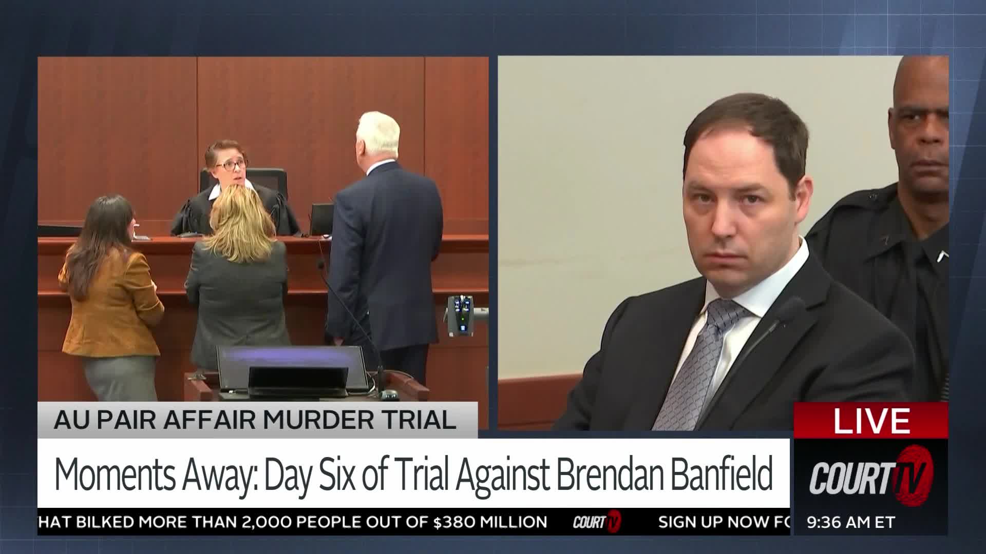 A judge in a black robe addresses two lawyers and a defendant in a courtroom. Beside them, a man in a dark suit sits with a serious expression, a uniformed officer standing behind him.