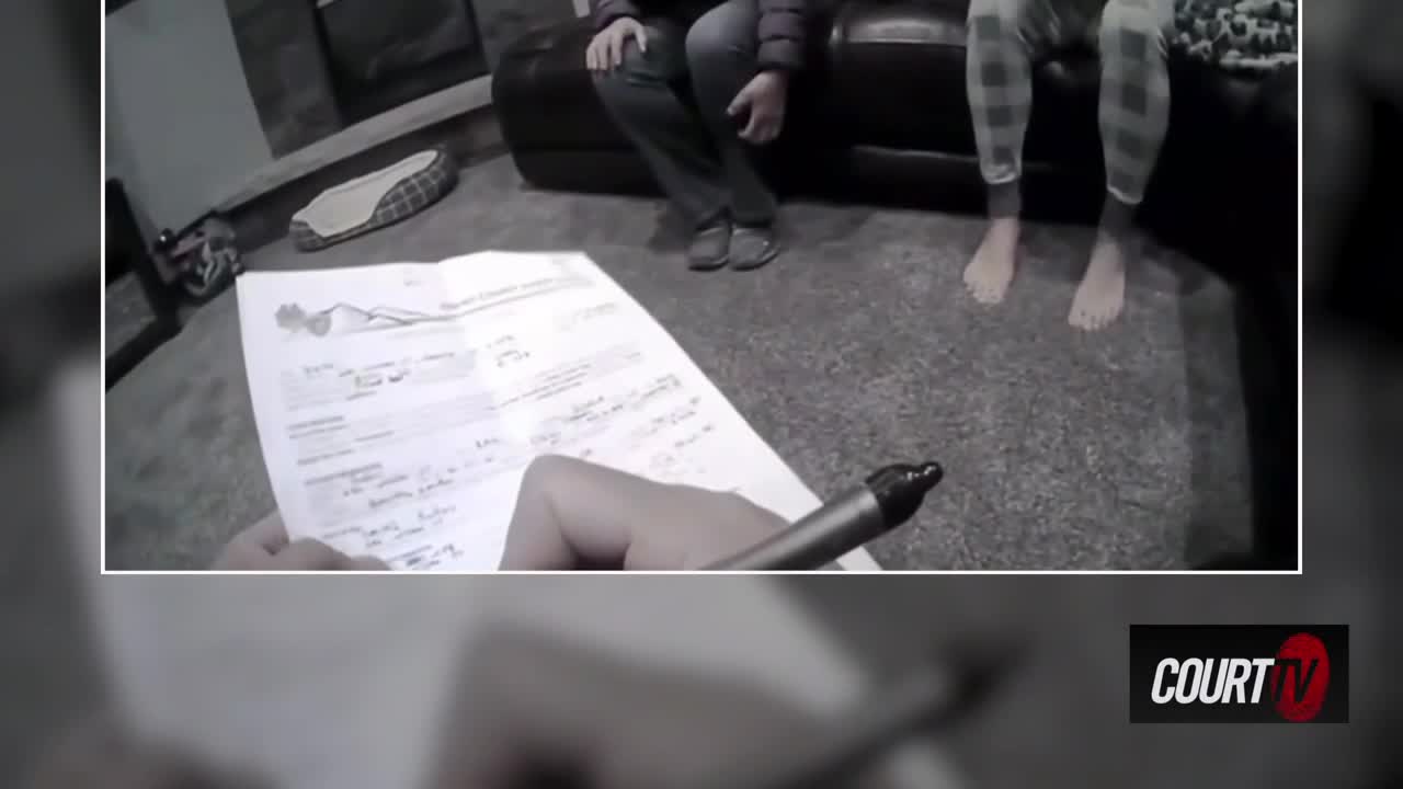 A hand grips a pen, poised over a document. Two people sit on a couch, their legs visible as they watch the proceedings.