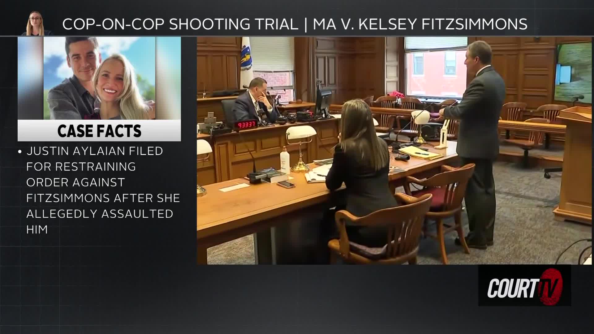 A man in a suit stands, gesturing towards a woman seated at a table. The judge, also in a suit, sits behind a large wooden desk, listening intently.