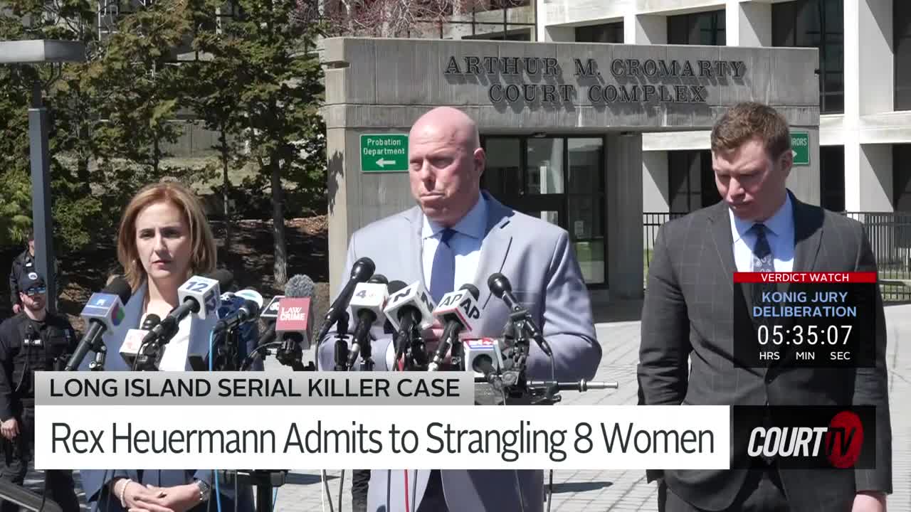 A woman in a light blue jacket stands at a podium, facing a wall of microphones. Behind her, a bald man in a grey suit speaks, his expression serious. To the right, another man in a dark suit walks away, a Court TV graphic overlaying his image.