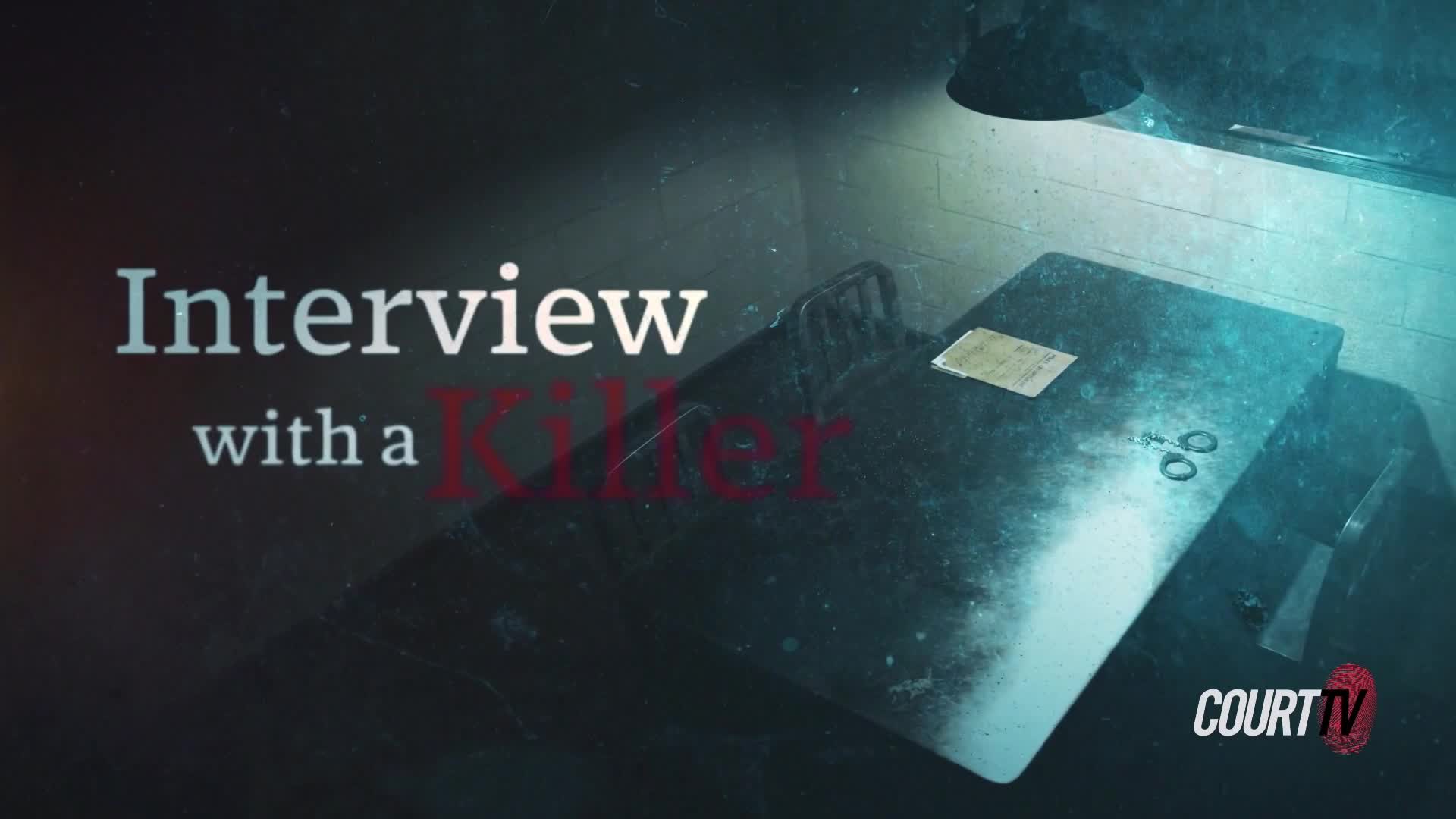 The stark interrogation room is lit by a single overhead lamp, casting long shadows across the metal table. A few papers and a pair of scissors rest on its surface, waiting for the interview to begin.