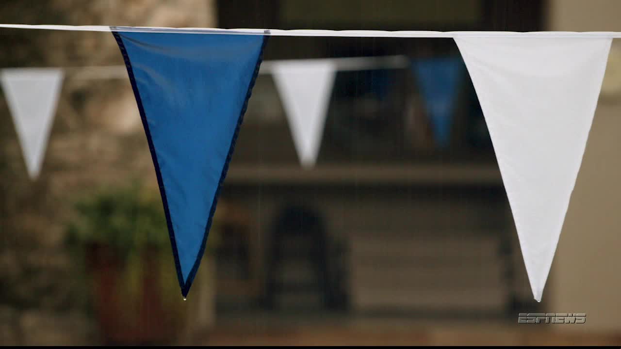 Triangular blue and white pennants hang from a taut line, gently swaying in the breeze. The background is blurred, but I can make out some buildings and greenery.
