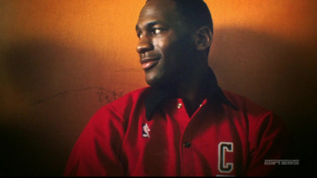 Michael Jordan, in a red Chicago Bulls jacket, glances to his right. The ESPNews logo is visible in the corner.
