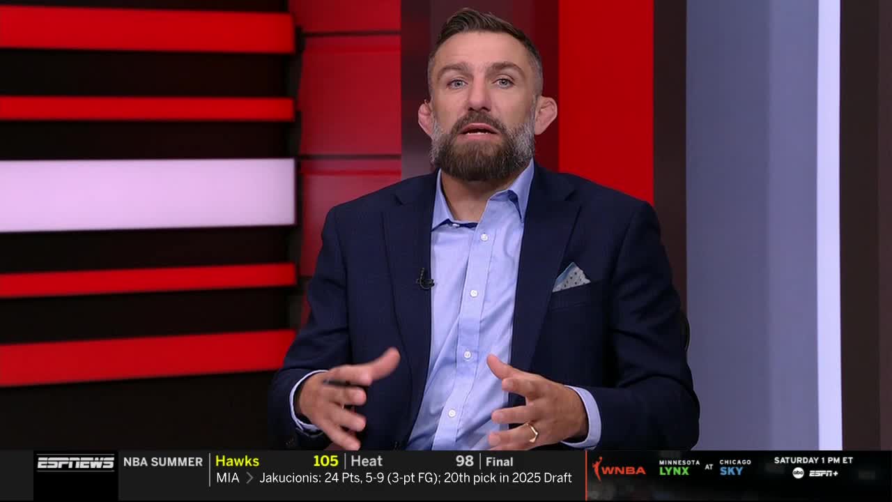 A man in a blue blazer gestures with his hands, talking on ESPNews. Behind him, a red and black graphic provides a backdrop for the broadcast.
