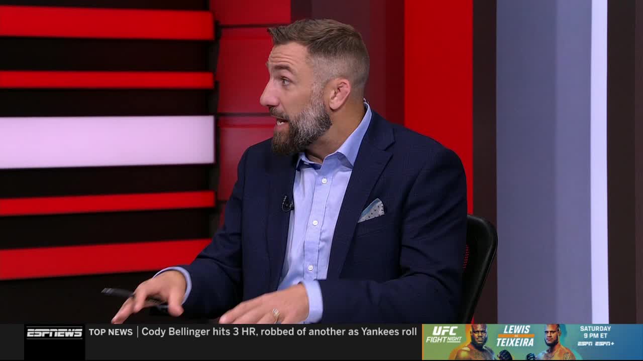 The man in the suit is gesturing with his left hand, speaking animatedly on ESPNews. Behind him, a red and black panel backdrop provides a stark contrast.
