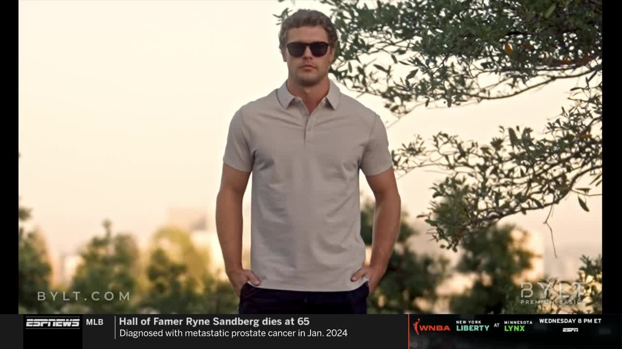 A man in sunglasses and a polo shirt stands with his hands in his pockets. The ESPNews banner at the bottom reports on Ryne Sandberg's death.
