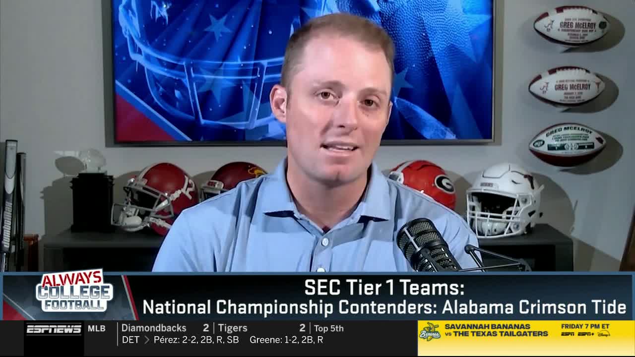 A man in a light blue shirt speaks into a microphone, discussing college football on ESPNews. Behind him, team helmets and footballs are displayed, with graphics indicating the SEC Tier 1 teams.
