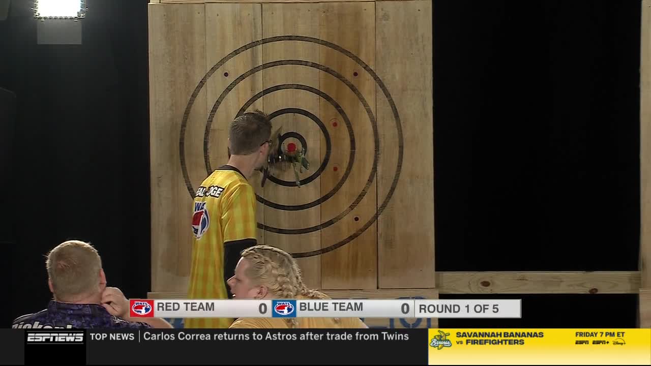 A competitor in a yellow jersey stands before a wooden target, inspecting the axes he's thrown. The score is tied at zero in round one of five, as shown on ESPNews.
