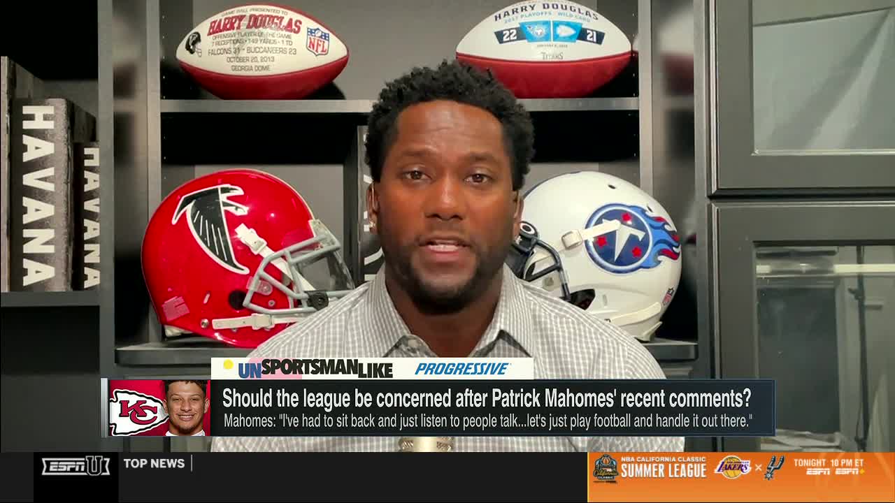 A man in a light-colored shirt is speaking, his gaze directed toward the camera. Behind him, shelves display football helmets and signed footballs, part of the set for ESPNU's "Unsportsmanlike."
