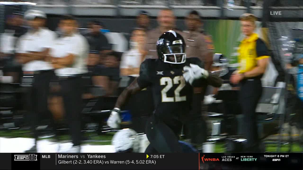 A player in a black and gold uniform, number 22, sprints toward the camera. The background is a blur of people and the edge of the field, all lit by stadium lights.
