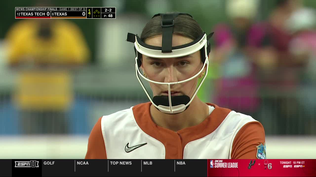 The Texas catcher, wearing a white and orange jersey, stares intently from behind her mask. The scoreboard on ESPNU shows the score tied in the WCWS Championship Finals.
