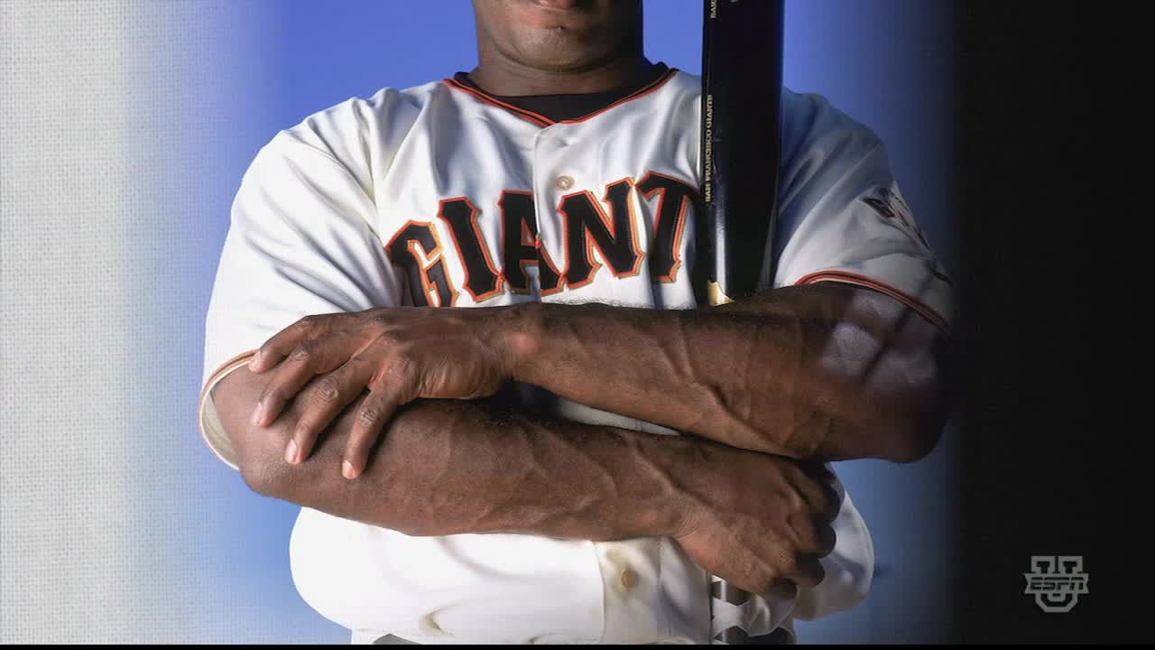 A baseball player in a Giants jersey stands with his arms crossed, a bat resting against his shoulder. His heavily-veined forearms are on display, and the ESPN logo is visible in the corner.
