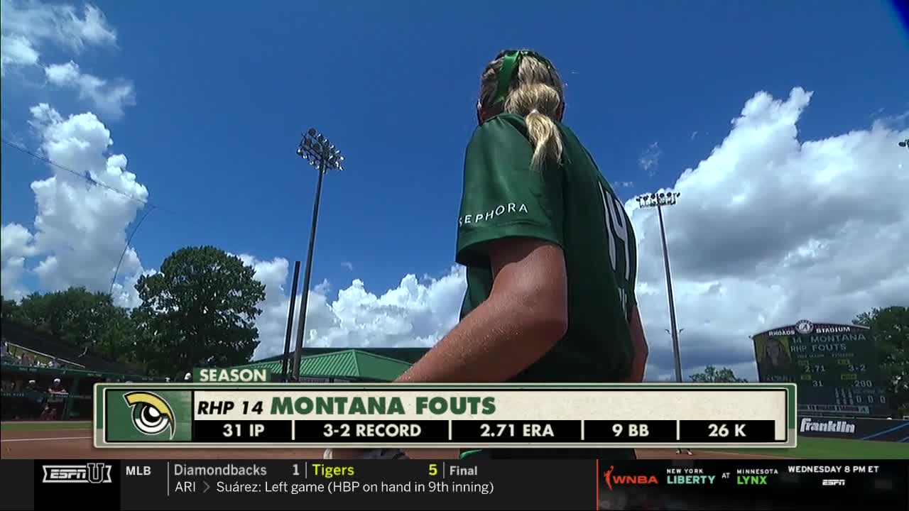 The pitcher, number 14, stands with her back to the camera, her green jersey contrasting with the bright sky. A scoreboard displays her stats as the game continues on ESPNU.
