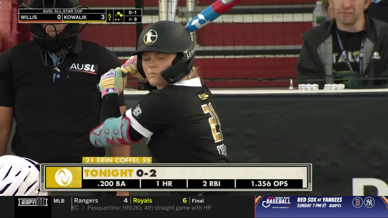 Erin Coffel, number 21, is at bat, her eyes fixed on the pitcher. The umpire, masked and stoic, watches from behind.
