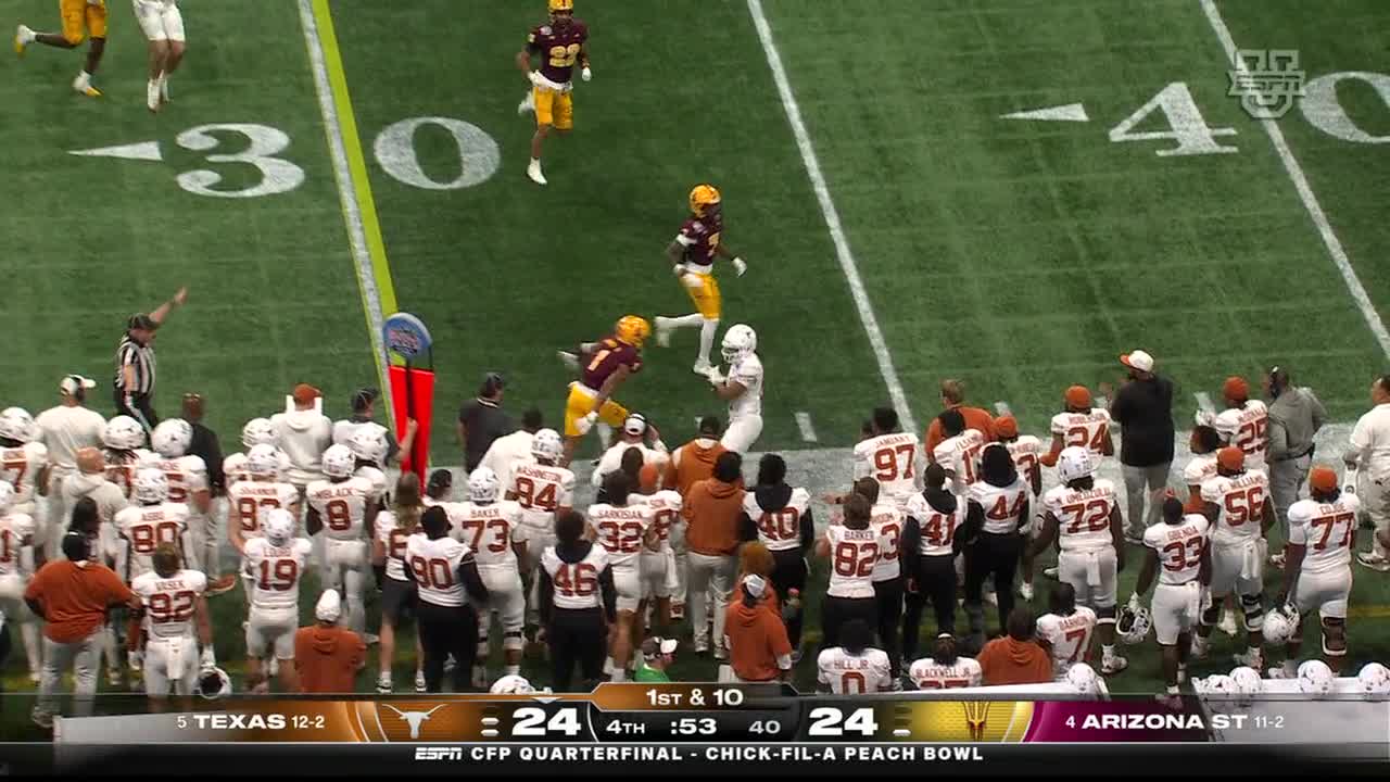 A player in white is about to be tackled by two players in maroon and gold. The Texas team, in white uniforms, watches from the sideline as the play unfolds on ESPNU.
