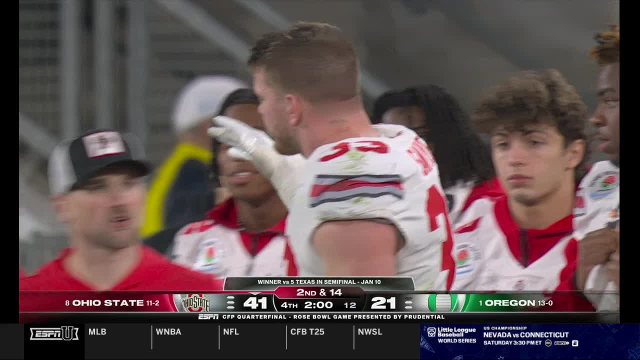 A player in a white and red jersey gestures towards his teammates, his arm extended. The scoreboard on ESPNU shows Ohio State leading Oregon in the fourth quarter of a CFP Quarterfinal.
