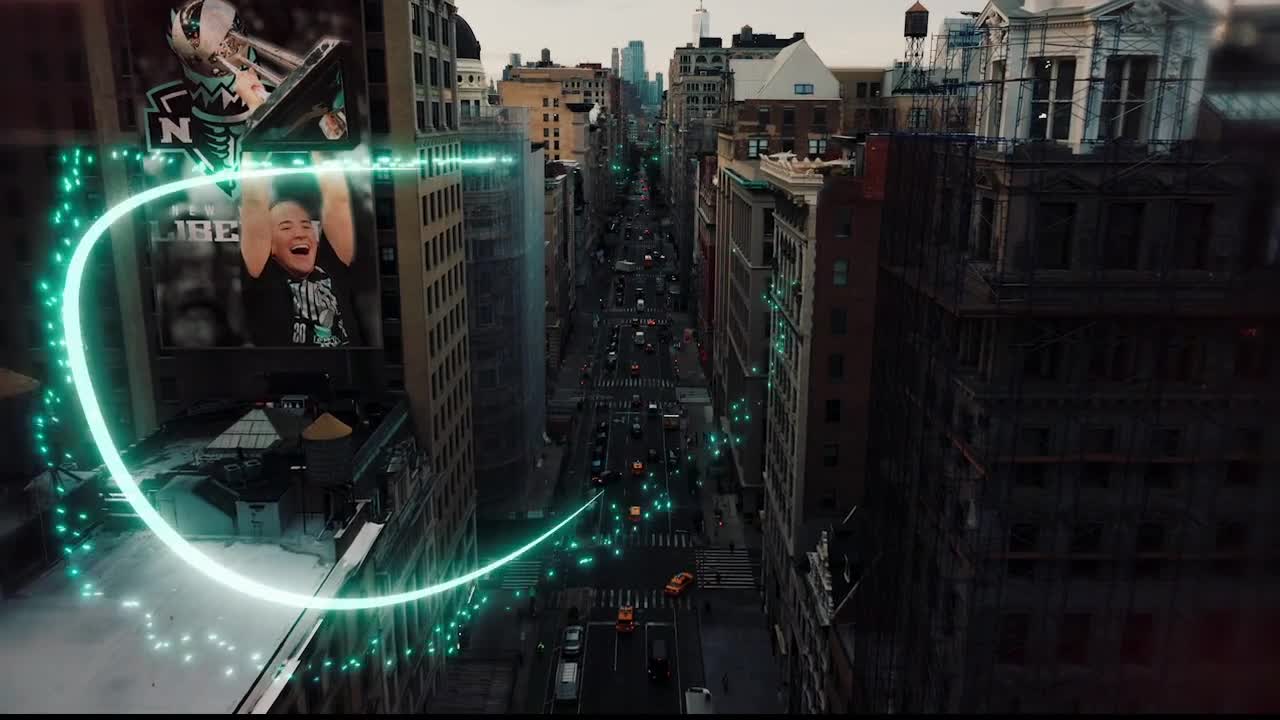 A glowing green line arcs over a New York City street, while a billboard shows a joyous athlete. Cars and trucks move slowly down the avenue below, framed by tall buildings.
