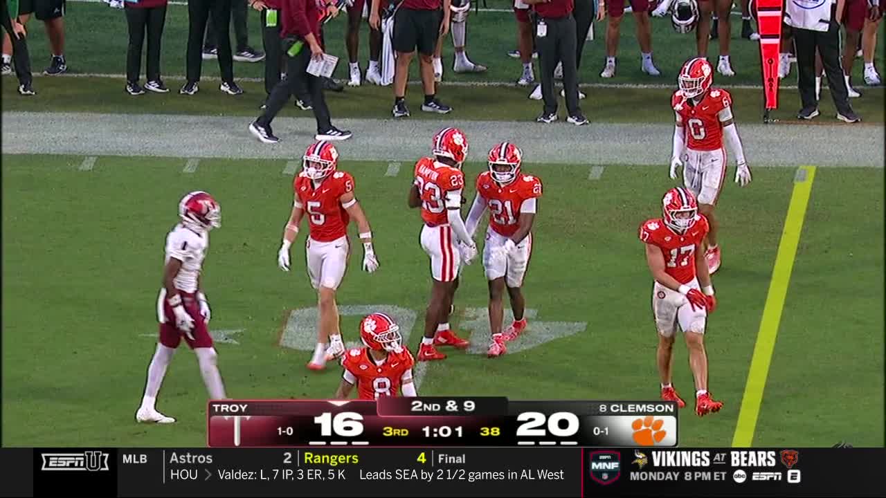 Players in red and white uniforms are gathered on the field, a player from the opposing team in white and maroon walks away. The scoreboard on ESPNU shows Clemson leading Troy in the third quarter.
