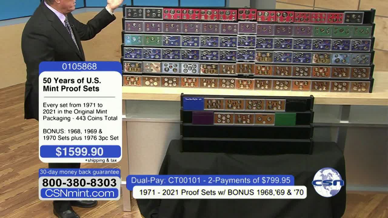 A man in a suit gestures toward a display of coin sets, stacked in rows. The Fox Business Network broadcast promotes a collection of U.S. Mint proof sets for sale.
