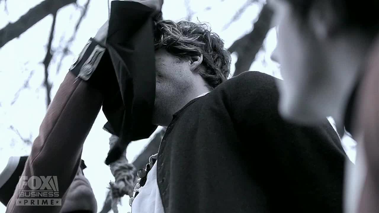 A man in a dark coat is lifting his hat, obscuring his face. The Fox Business Network logo is visible in the corner.
