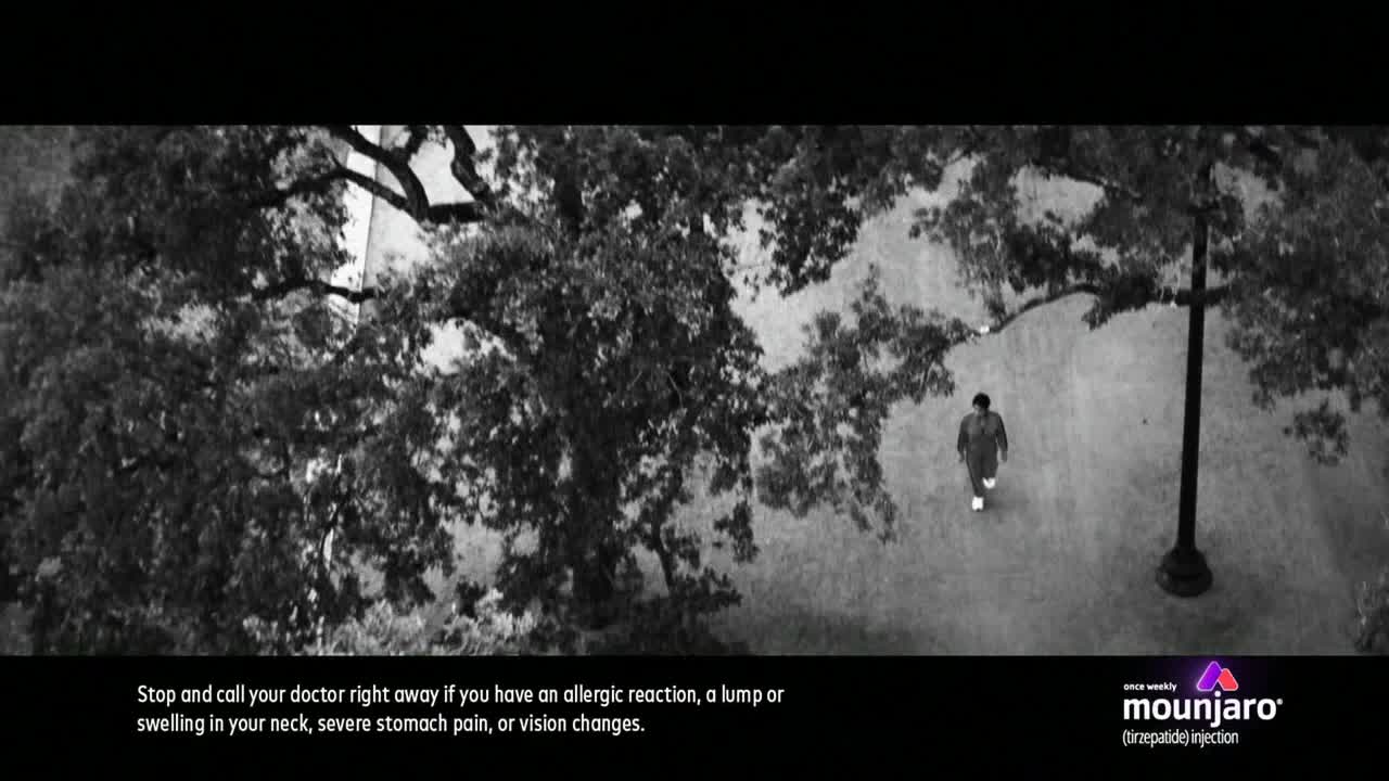 A lone figure walks down a path, the scene framed by a large tree and a lamppost. The commercial, likely airing on Fox Business Network in the United States, warns about potential side effects.
