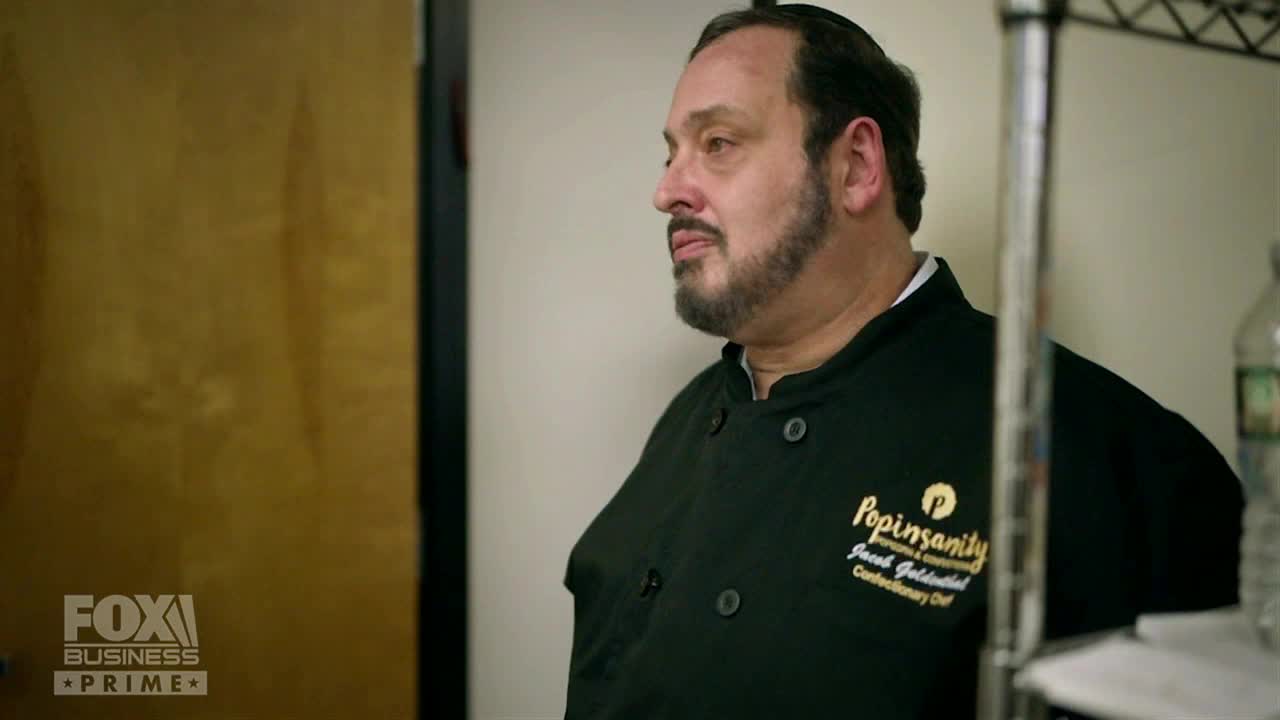 A man in a black chef's coat stands in a commercial kitchen, looking off-camera. The Fox Business Network logo is visible in the corner of the screen.
